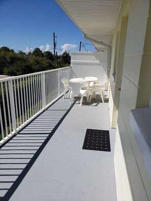 A balcony with a white railing, a small table with chairs, and a white wall. - Studio 1 Motel (Daytona Beach)