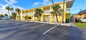 A yellow motel with a parking lot, palm trees, and a white car parked outside. - Studio 1 Motel (Daytona Beach)