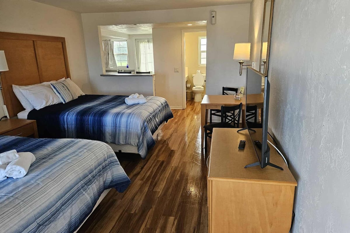 A hotel room with two beds, a wooden desk, a chair, a table, and a mirror.