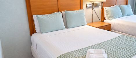 A hotel room with two beds, a wooden headboard, a nightstand with a lamp, and a patterned bedspread.