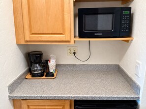 A kitchen with a microwave on a wooden shelf, a coffee maker on the counter, and a power outlet. - Studio 1 Motel (Daytona Beach)