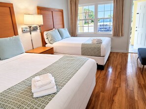 A hotel room with two beds, a nightstand, a lamp, and a window with curtains.