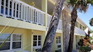 A two-story motel with a yellow facade, white railings, and a small outdoor seating area with a white chair. - Studio 1 Motel (Daytona Beach)