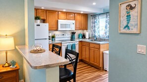 A kitchen with wooden cabinets, a microwave, a stove, and a sink. - Studio 1 Motel (Daytona Beach)