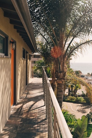 Un balcón con vista al mar, una palmera y un edificio con suelo de baldosas.