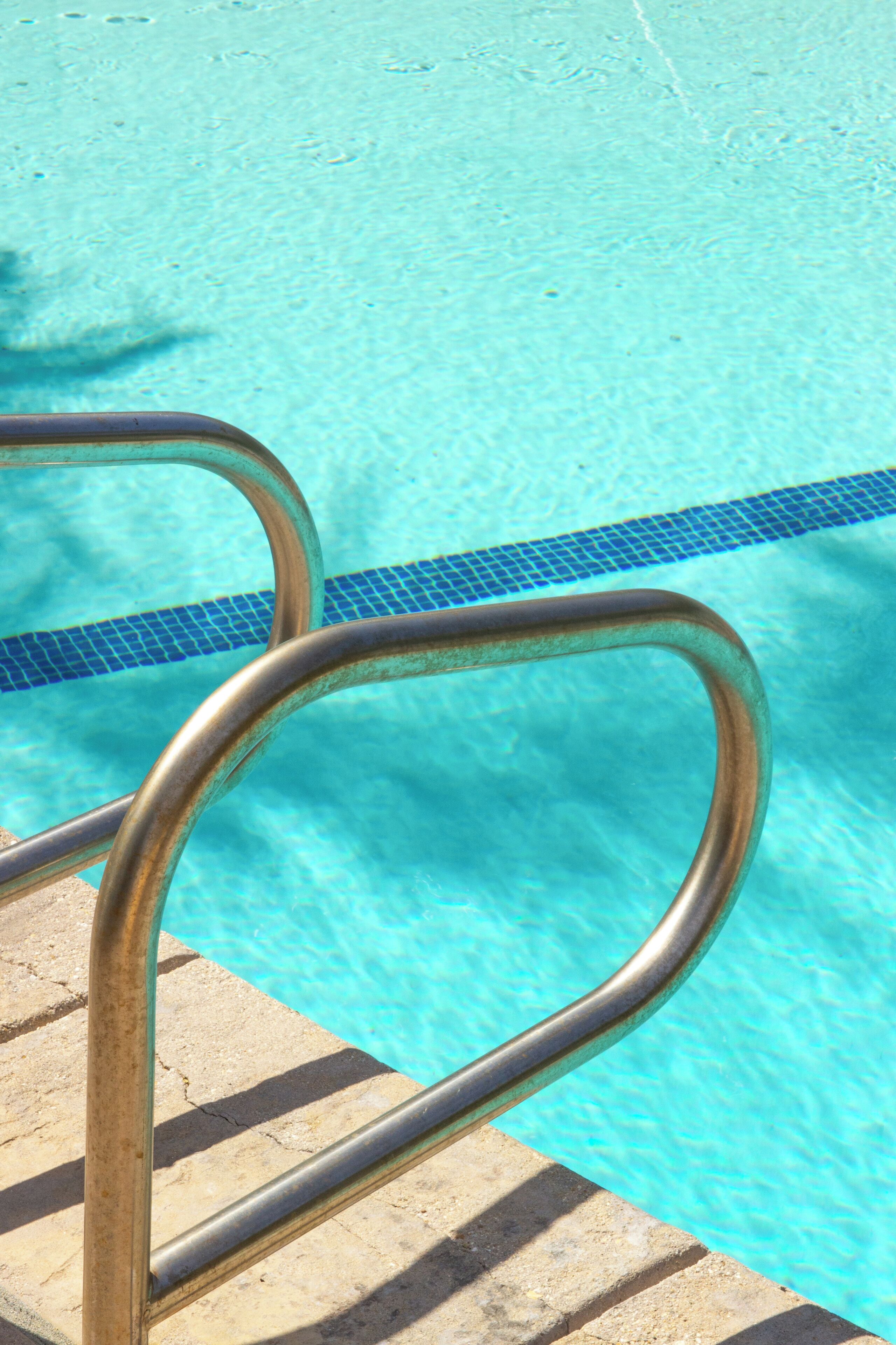 A metal pool ladder leading into a clear blue pool with a tiled edge.
