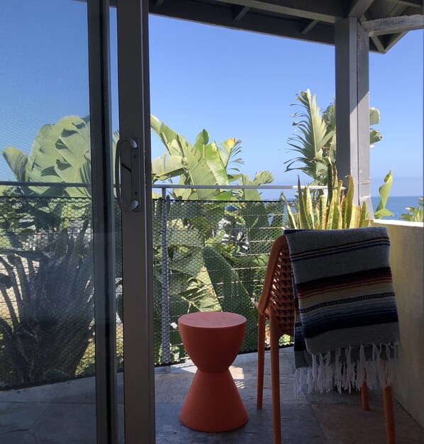 A balcony with a view of the ocean, a red chair, and a striped towel. - The Malibu Motel (Malibu)