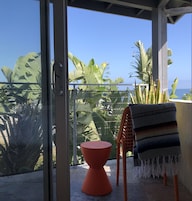 Un balcón con vistas al océano, una silla roja y una toalla a rayas.