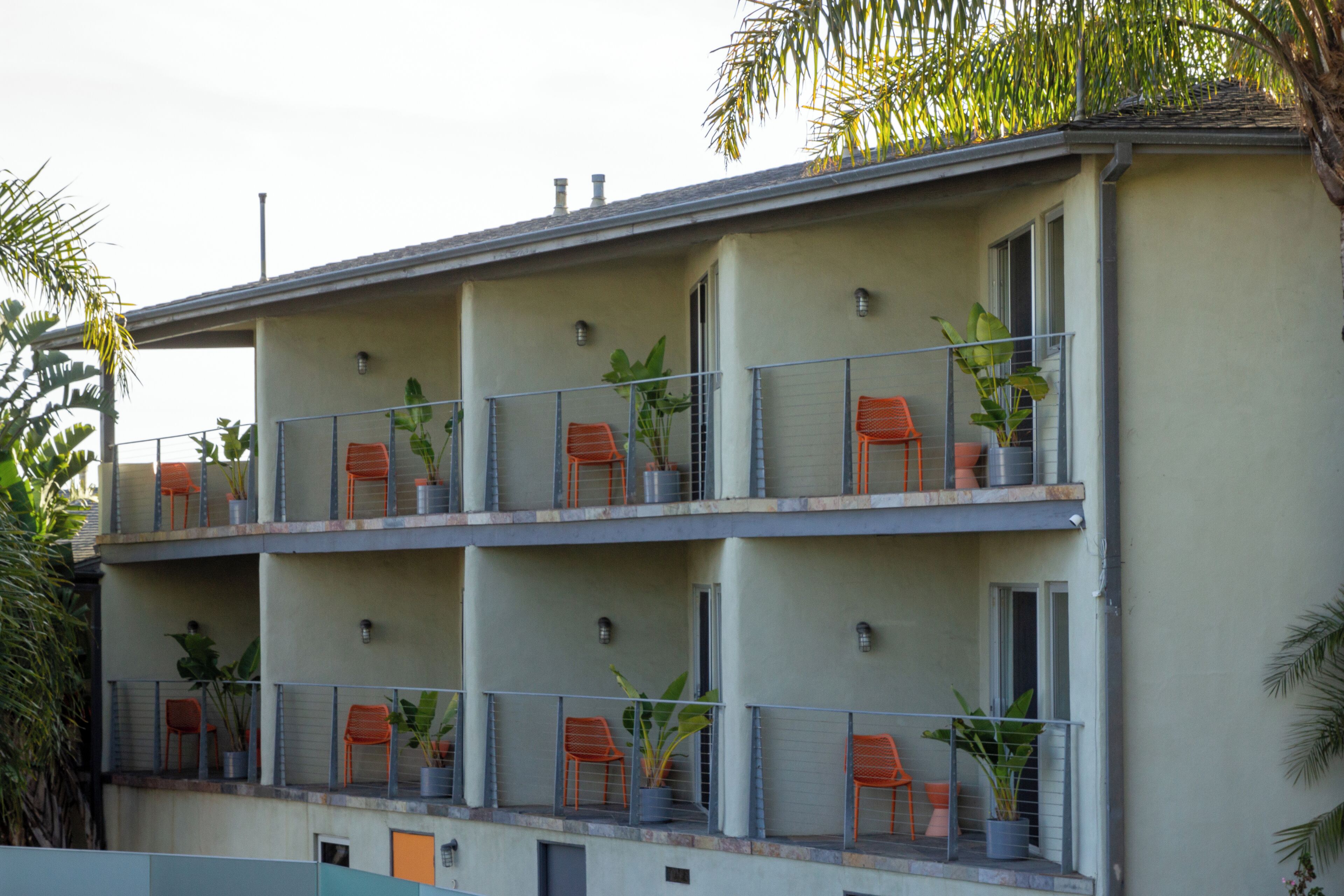 Un edificio de varios pisos con balcones, plantas en macetas y sillas naranjas.