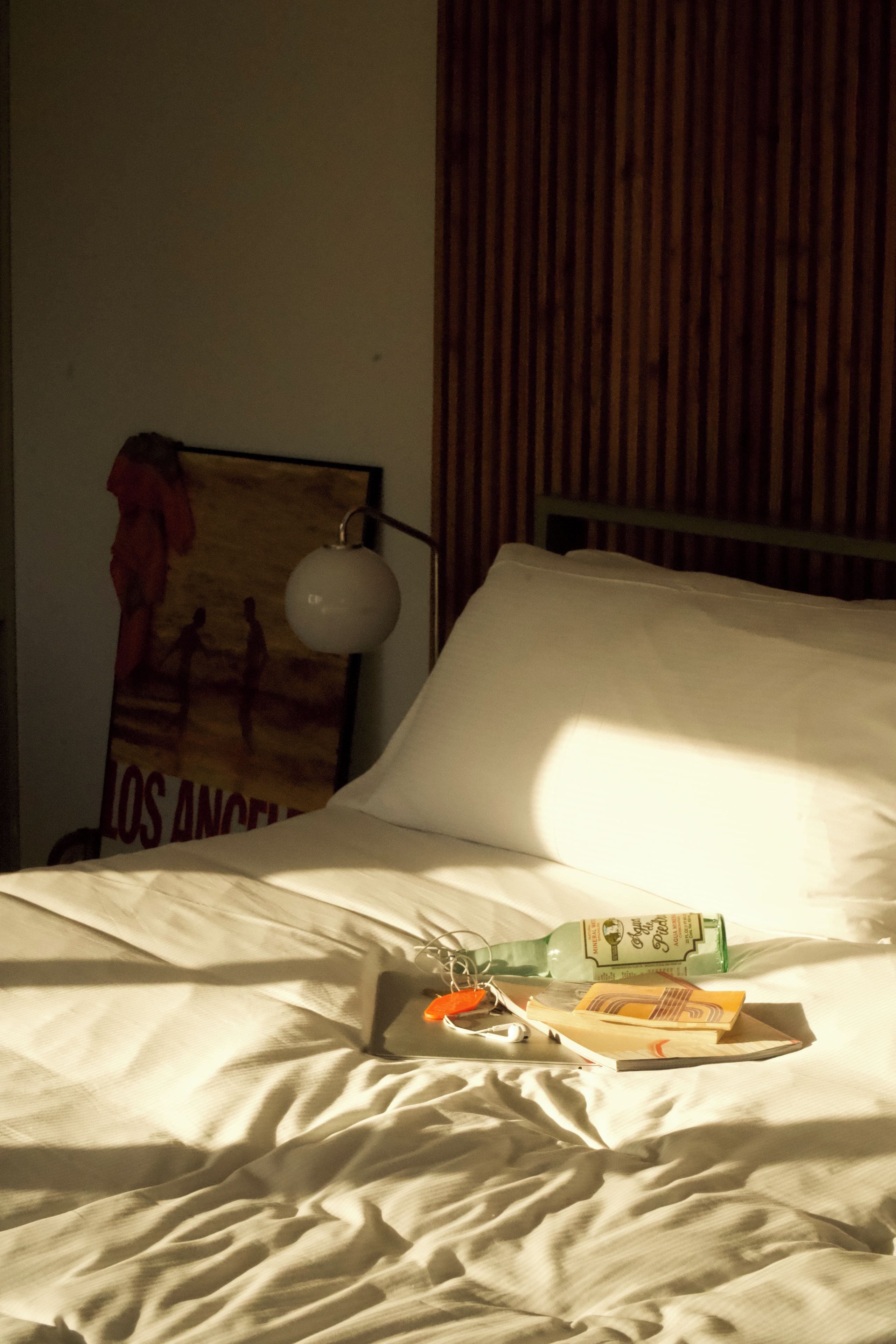 Una cama con almohada y manta, un cartel en la pared y una botella sobre la cama.