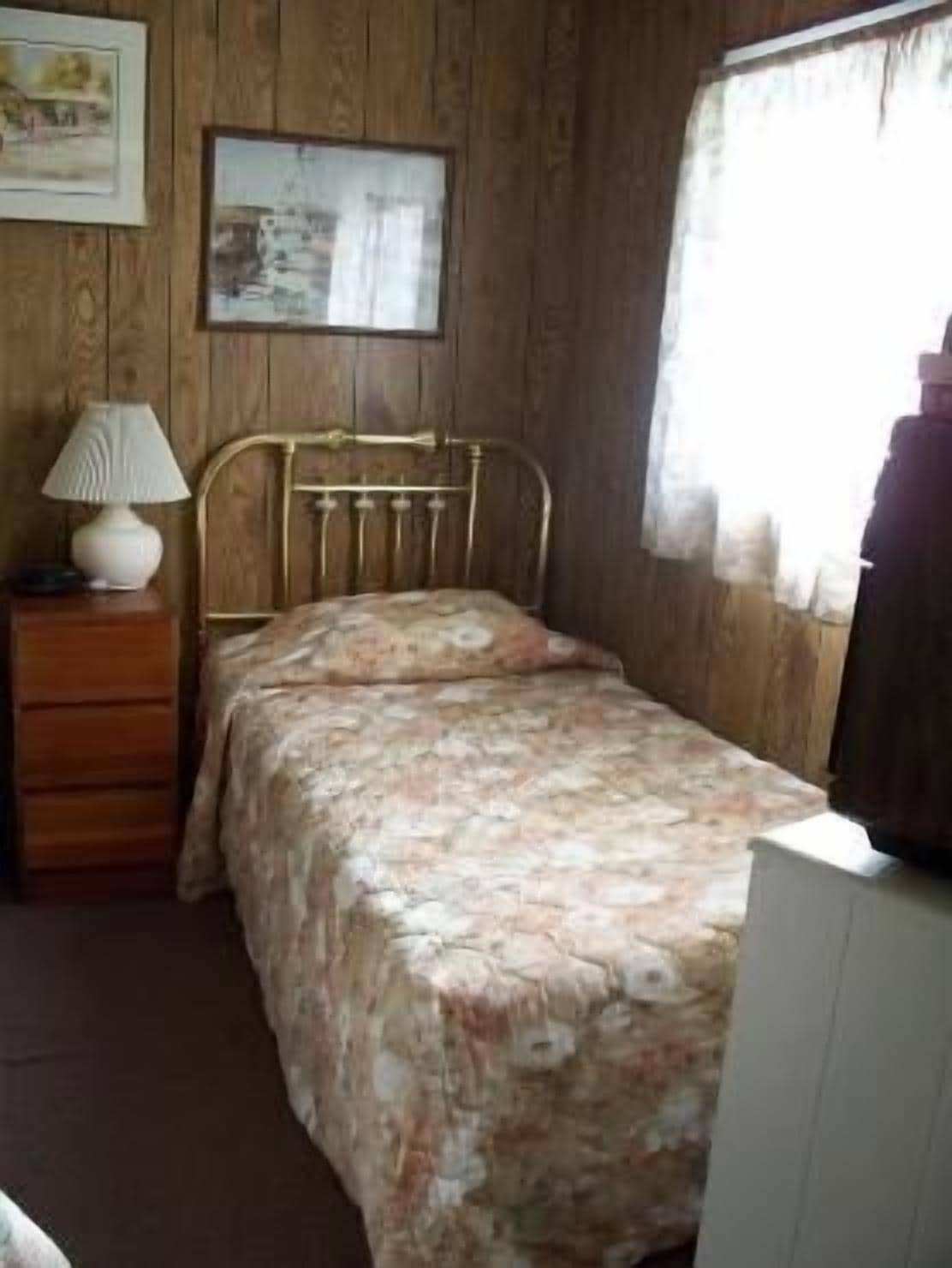 A room with a bed, a dresser, a lamp, and a window with curtains.