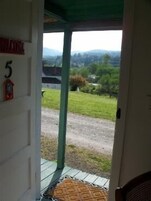 A room with a door leading to a covered outdoor area with a view of a grassy landscape and hills.