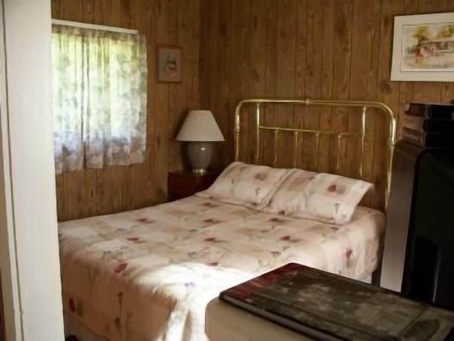 A single bed with a floral bedspread, a bedside lamp, and a framed picture on the wall.