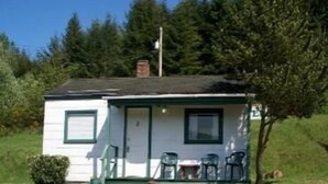 A small, single-story cabin with a green door and windows, a chimney, and a porch with outdoor furniture. - Valley View Motel (Port Townsend)