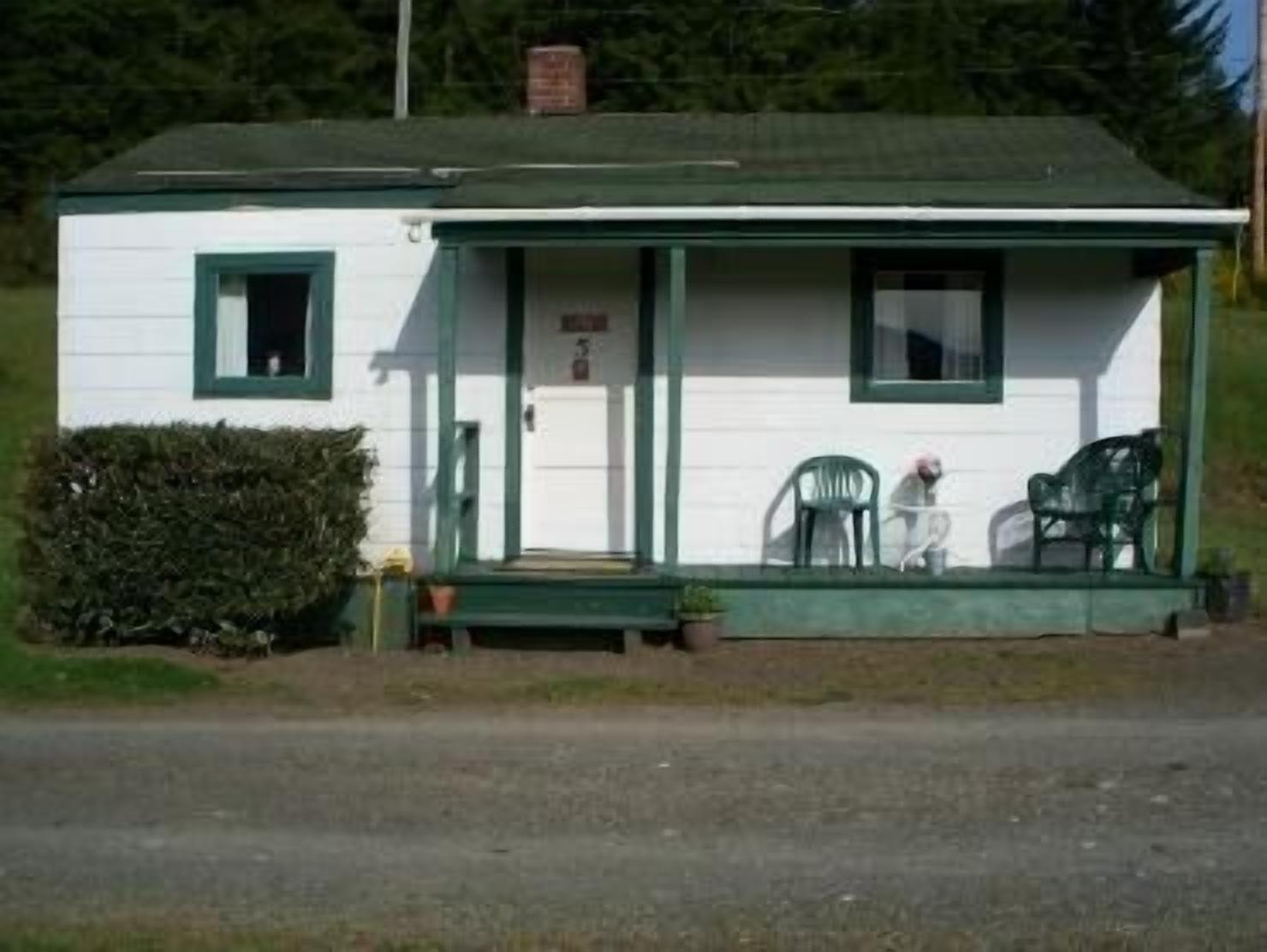 A small, single-story building with a porch, a door, and two chairs outside.