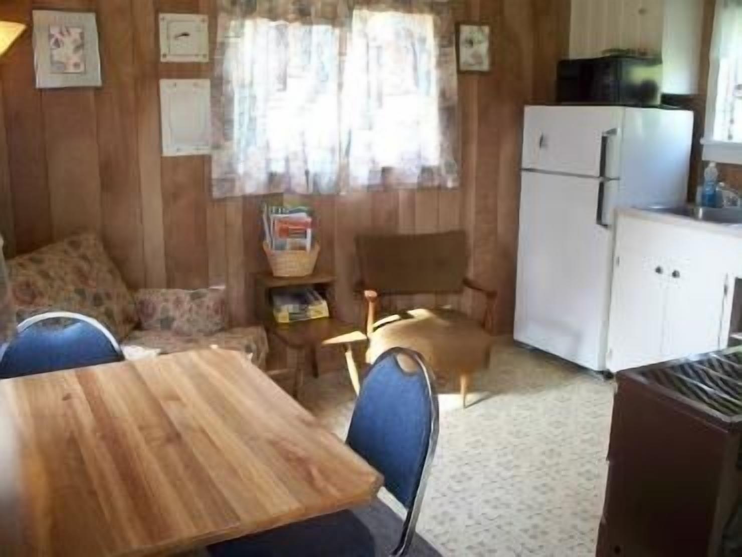 Una habitación compacta con una mesa de madera, dos sillas, un sofá, un mueble pequeño y un refrigerador.