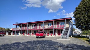 Un motel à la façade rouge et blanche, avec un camion rouge garé devant et un escalier menant à l’étage supérieur.