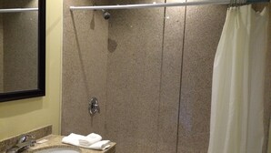 Une salle de bain avec un lavabo sur un plan de travail en granit, un miroir, une douche avec un rideau et une baignoire.