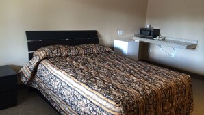Une chambre avec un lit, une table de chevet, un four à micro-ondes et une petite étagère.