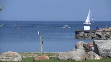 Paisaje costero con un velero, rocas grandes y un muelle de madera.