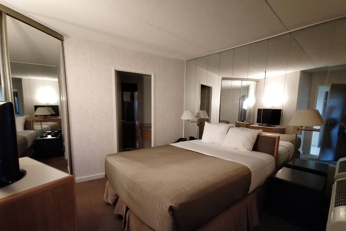 A hotel room with a large bed, bedside tables, a TV, a mirror, and a wardrobe.