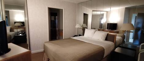 Een hotelkamer met een groot bed, nachtkastjes, een televisie, een spiegel en een kledingkast.