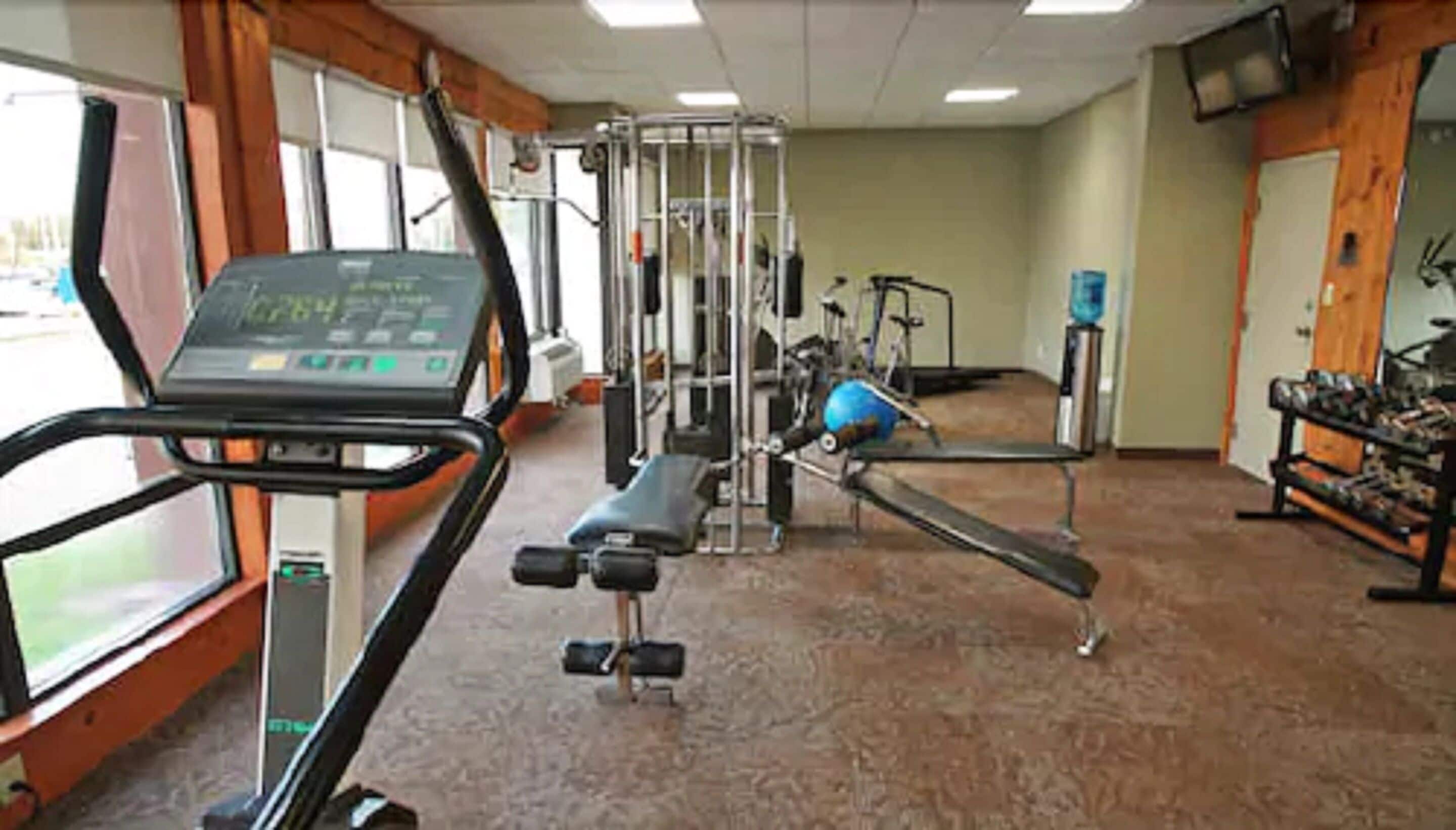 Ein Fitnessstudio mit Cardiogeräten, Krafttrainingsgeräten und einem an der Wand befestigten Fernseher.
