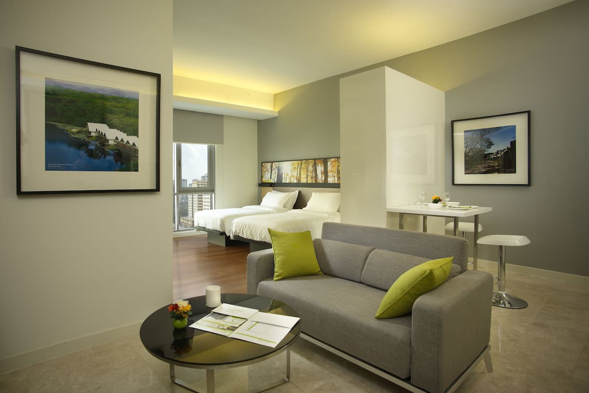 Ein modernes Hotelzimmer mit einem Bett, einem grauen Sofa, einem kleinen Tisch mit Blumen und gerahmten Bildern an den Wänden.