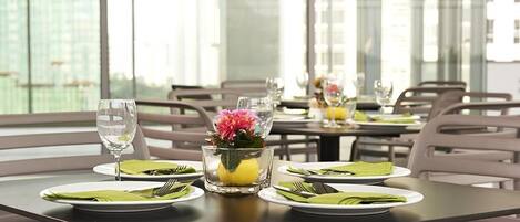 A dining area with tables set for two, featuring clear glassware and green napkins.