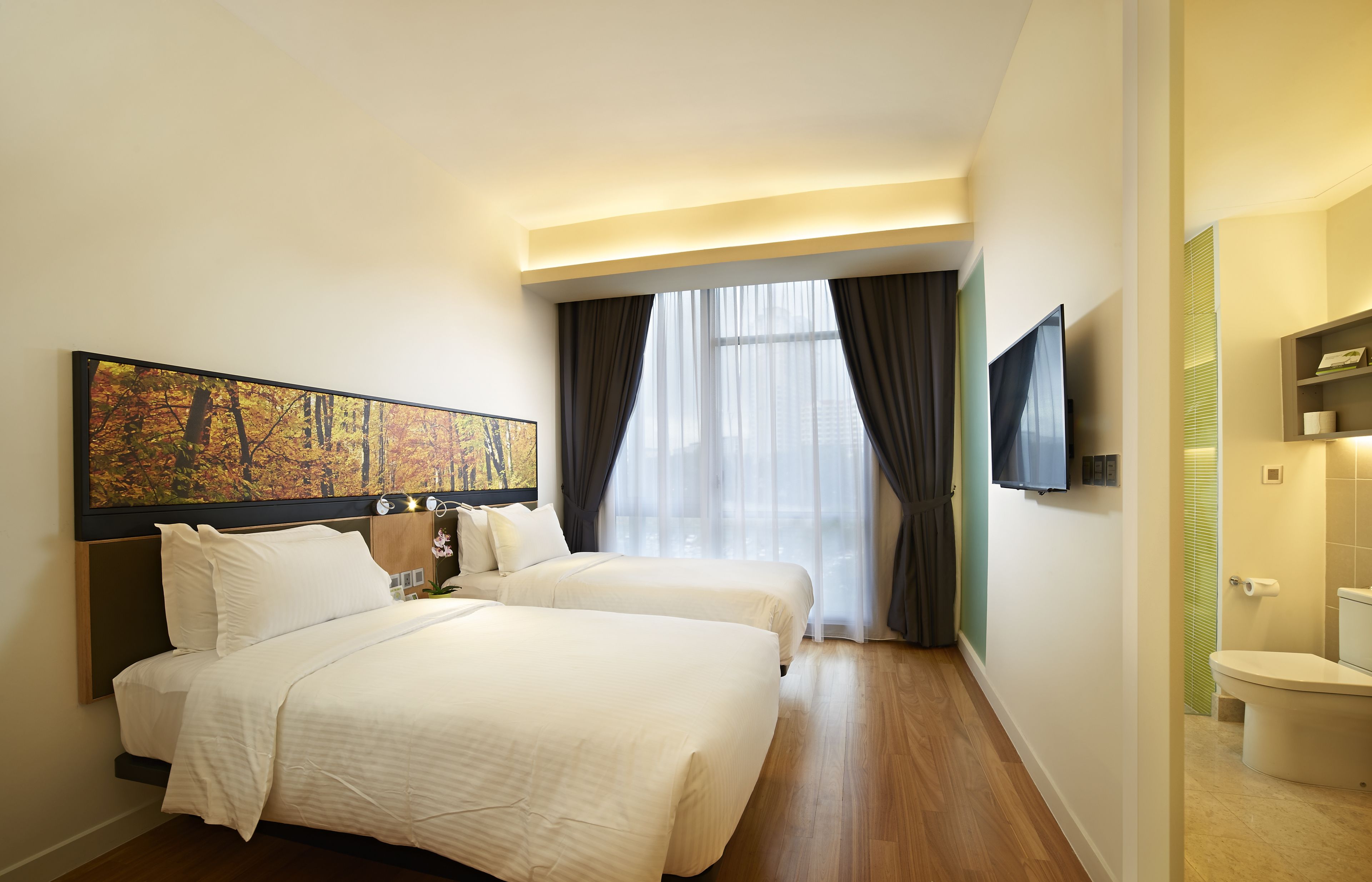 A hotel room with two beds, a large painting, a TV, and a bathroom.