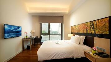 A hotel room with a large bed, a desk, a chair, a TV, and a window with a city view.