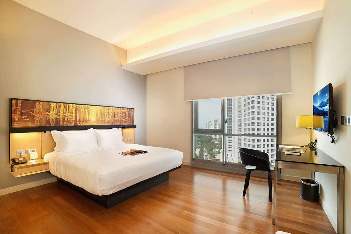 Ein modernes Hotelzimmer mit einem großen Bett, einem Schreibtisch mit Stuhl, einem Fernseher und einem großen Fenster mit Blick auf die Stadt.