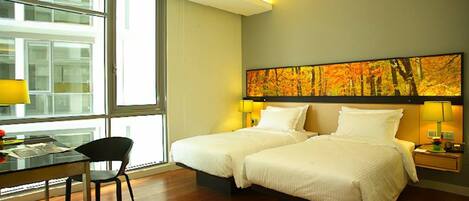 A hotel room with two beds, a desk with a chair, and a large window.