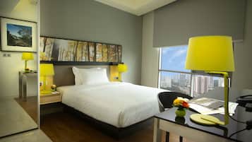 Una habitación de hotel moderna con una cama grande, dos mesitas de noche con lámparas, un escritorio con una silla y un ventanal con vistas a la ciudad.