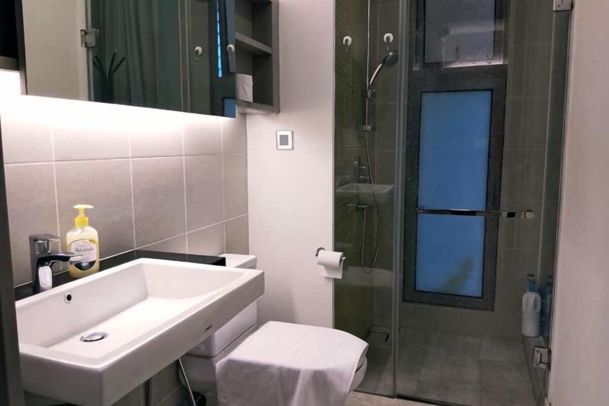 Baño con lavamanos, espejo, toalla y zona de ducha.