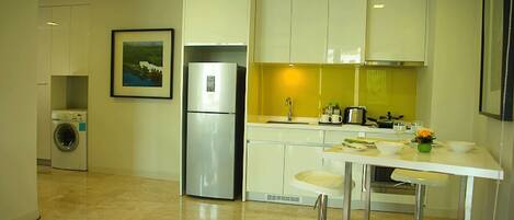 A modern kitchen with white cabinets, a stainless steel refrigerator, a washing machine, and a bar area with stools.