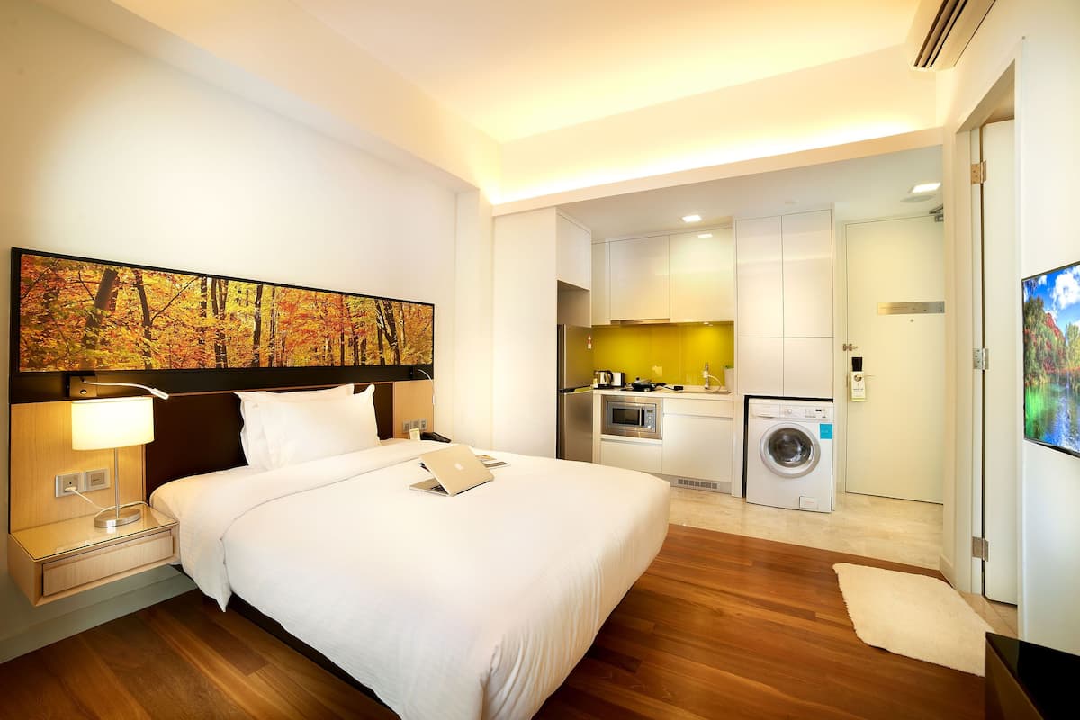 Ein Hotelzimmer mit Bett, Schreibtisch mit Laptop, Waschmaschine und einer Küchenzeile.