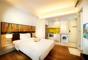 A hotel room with a bed, a desk with a laptop, a washing machine, and a kitchenette.