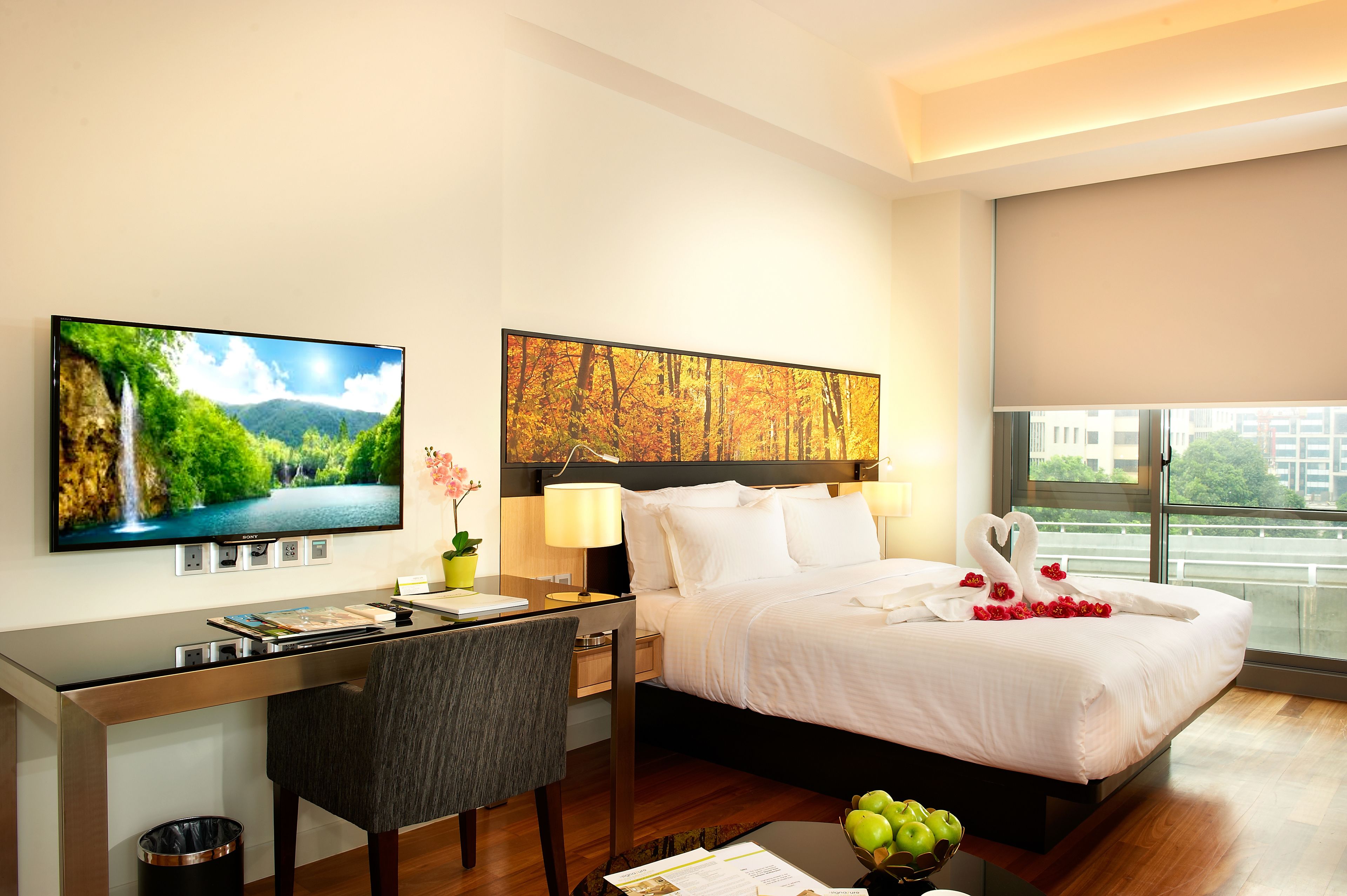 Hotelkamer met een bed, bureau, stoel, televisie, kunstwerken en een raam met uitzicht.