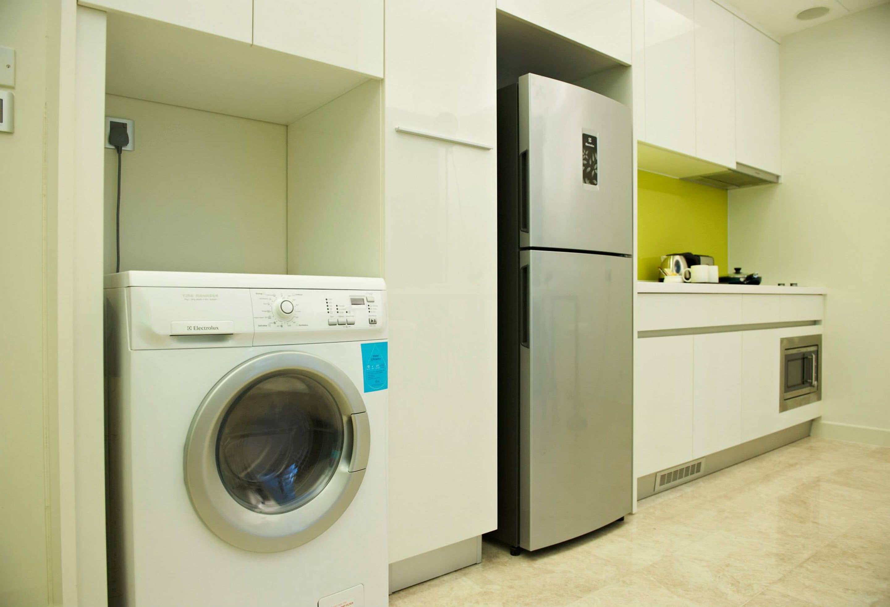 A compact kitchen with a washing machine, a refrigerator, and a microwave.