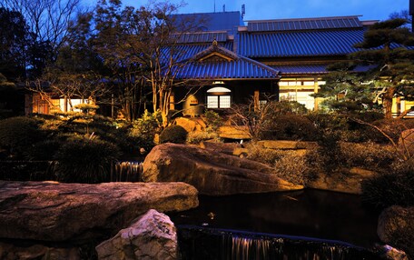 Un edificio japonés tradicional con techo de tejas, rodeado de rocas y un estanque.