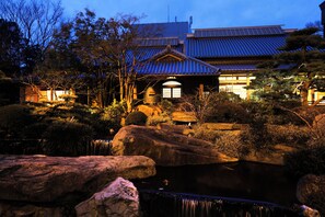 Un edificio japonés tradicional con techo de tejas, rodeado de rocas y un estanque.