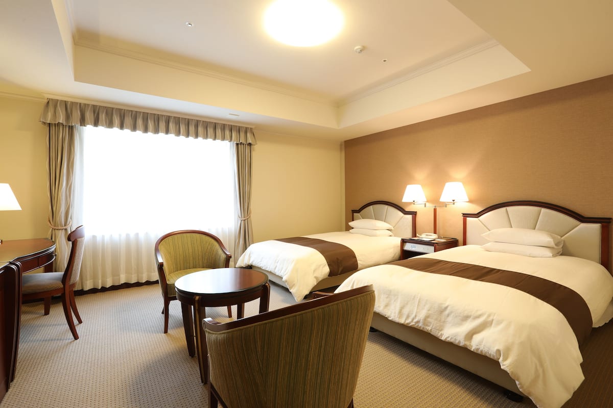 A hotel room with two beds, a desk, a chair, and a window with curtains.