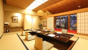 A traditional Japanese-style room with tatami flooring, a low table set for dining, and sliding doors leading to a view of trees. - Imabari Kokusai Hotel (Imabari)
