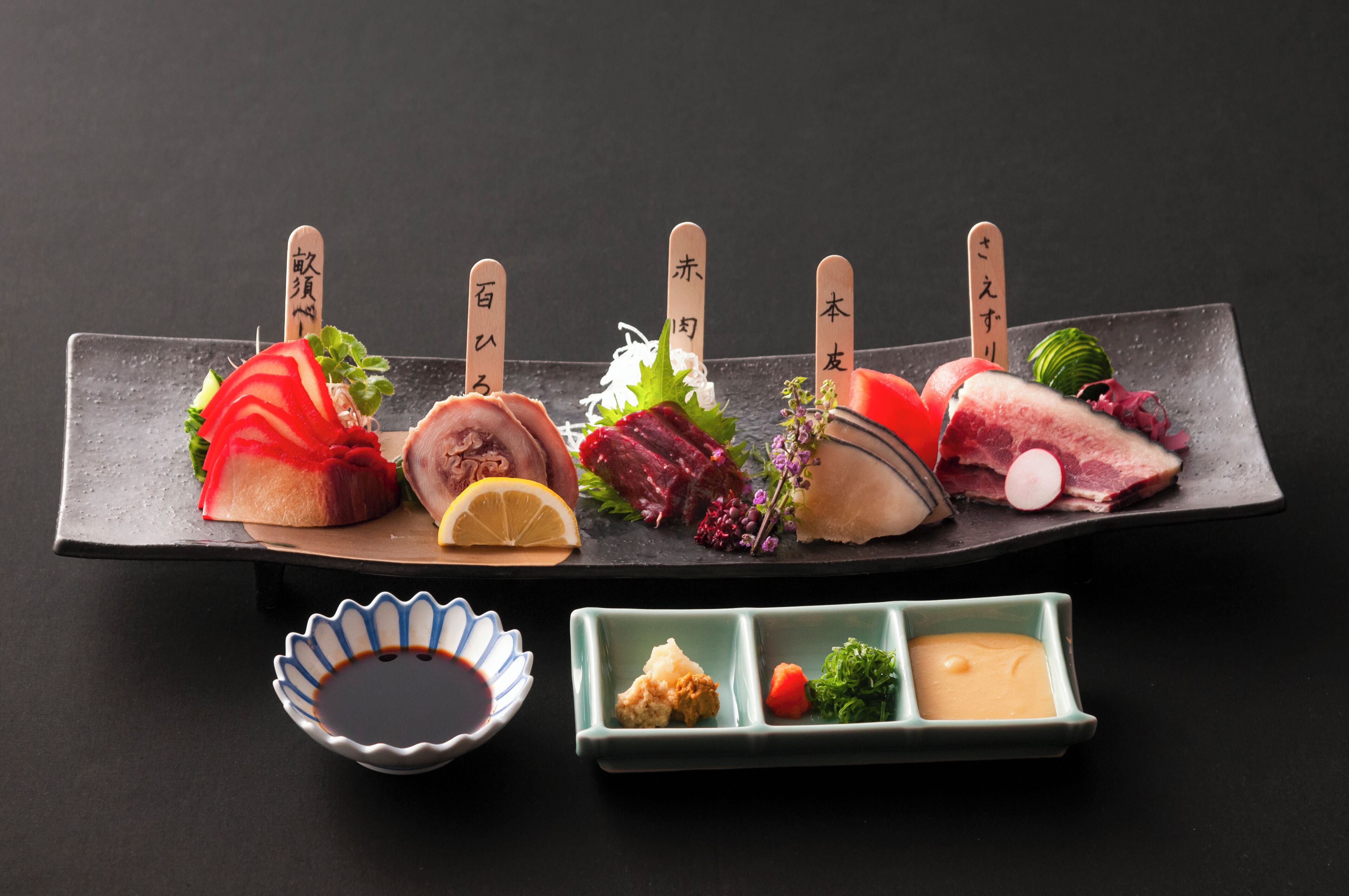 Un plateau de sushis comprenant différents types de poissons et diverses garnitures, accompagné de petits ramequins de sauce soja et de wasabi.