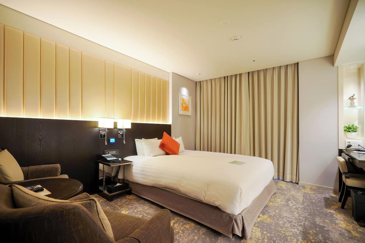 Una habitación de hotel con una cama grande, un escritorio con una silla, un sofá y una mesita de noche con una lámpara.