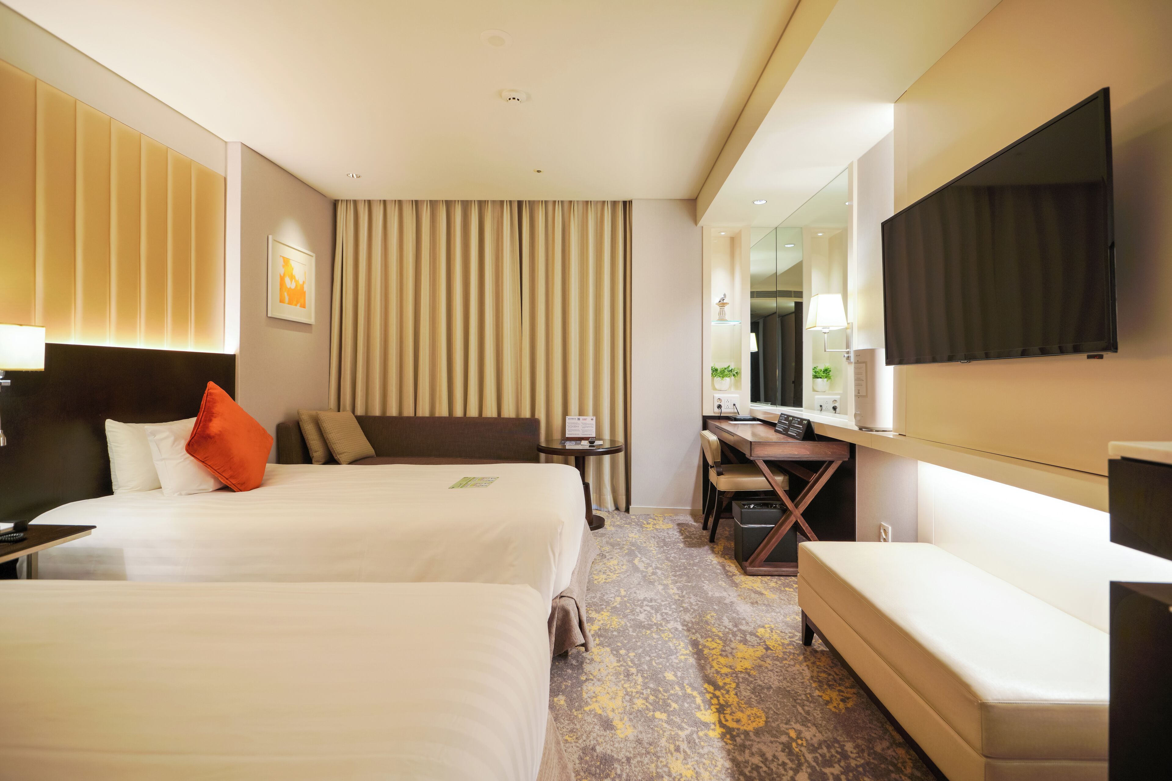 A hotel room with two beds, a desk, a chair, a TV, and a bathroom.
