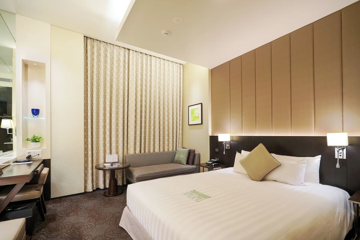 Una habitación de hotel con una cama grande, un escritorio con silla, una mesita y un sofá.