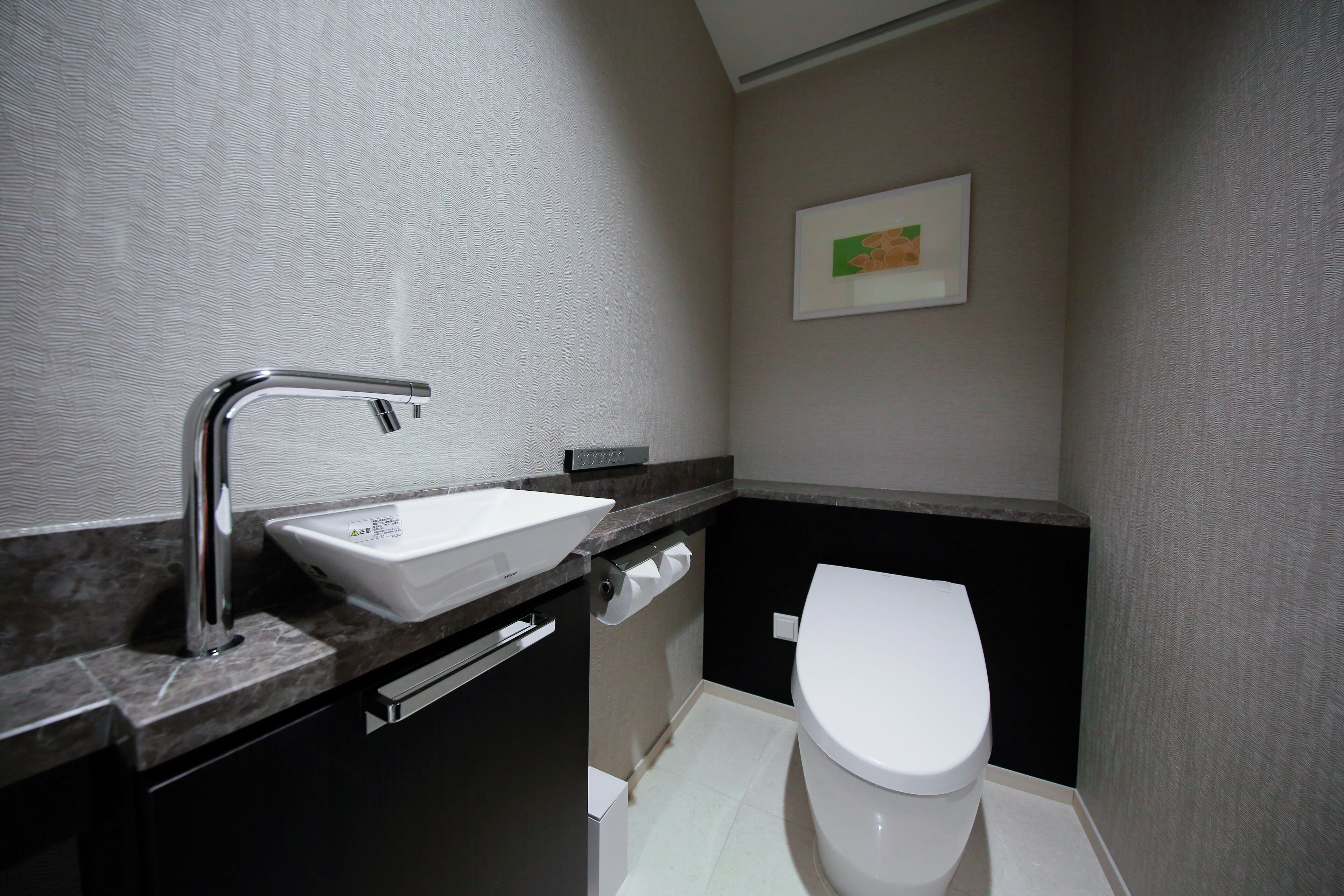 A modern bathroom with a white sink, chrome faucet, and a toilet.