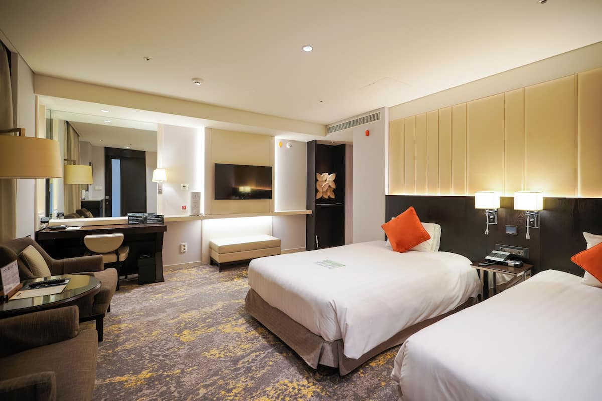 Habitación de hotel con dos camas, un escritorio, una silla, una mesita y un espejo.